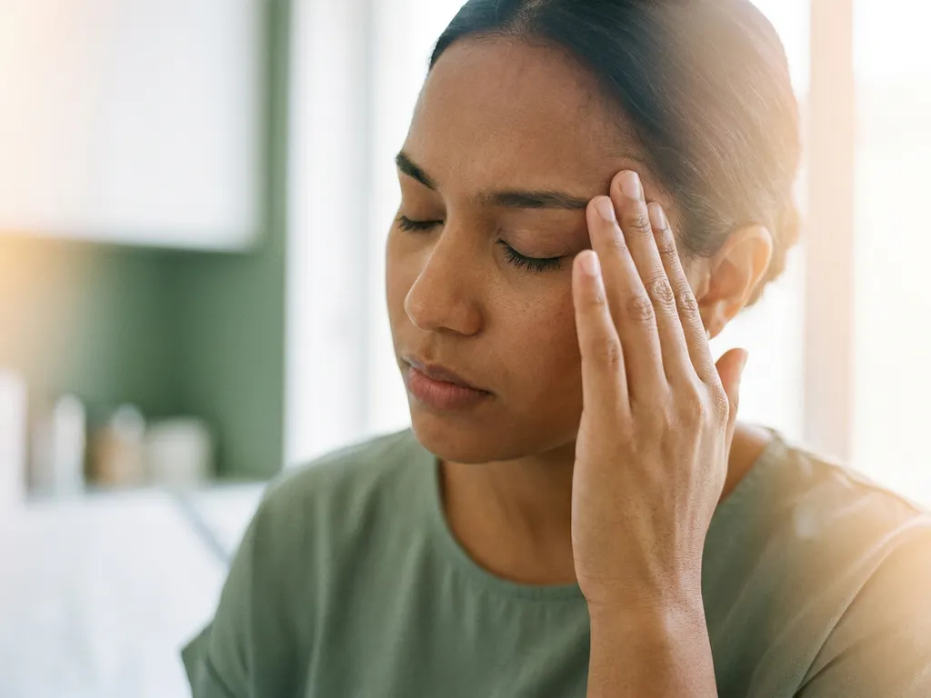 Persoon met gesloten ogen die vingertoppen tegen slaap drukt, met wazig lichteffect dat visuele migraine-aura suggereert.